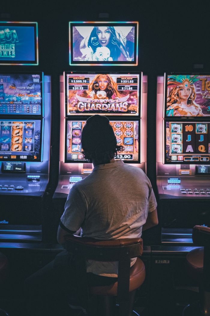 Adult male seated in a dimly lit casino engaging with vibrant slot machines at night.