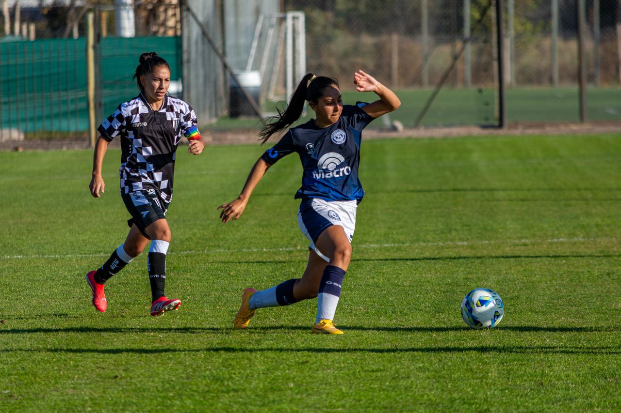 Home Action shot of female soccer players on a sunny outdoor field, capturing athleticism and competition.