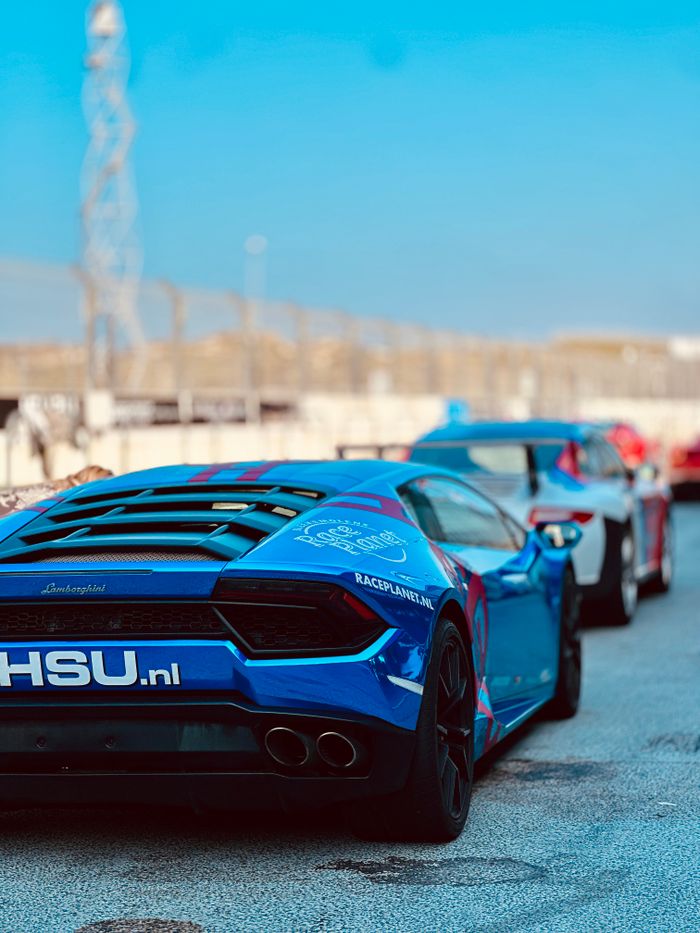 Services Rear view of colorful sports cars lined up on a race track under a clear blue sky.